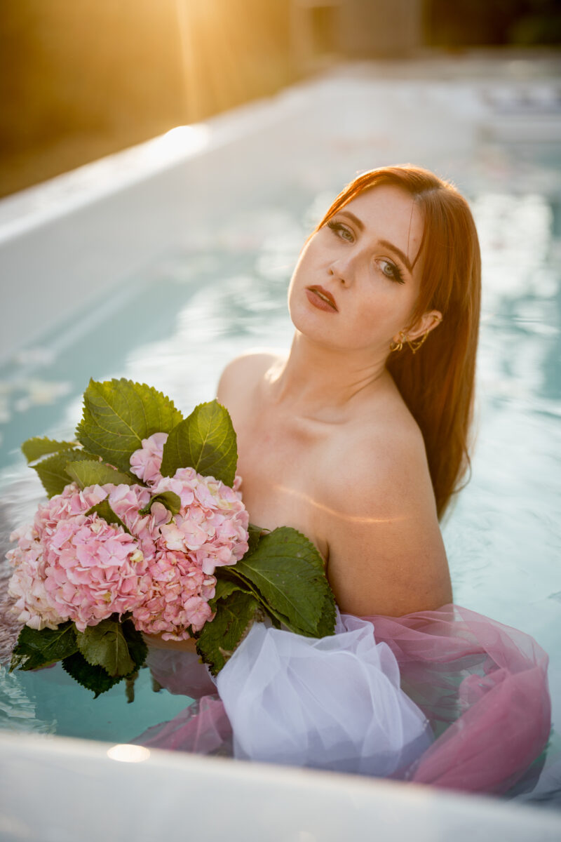 Akt- und Erotikfotografie Portfolio, rothaarige Frau mit rosafarbenem Blumenstrauß in Pool