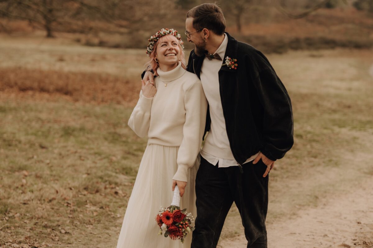 After Wedding, Braut und Bräutigam laufen einen Weg entlang. Er hat den Arm um sie gelegt. Beide schauen sich lächelnd an.