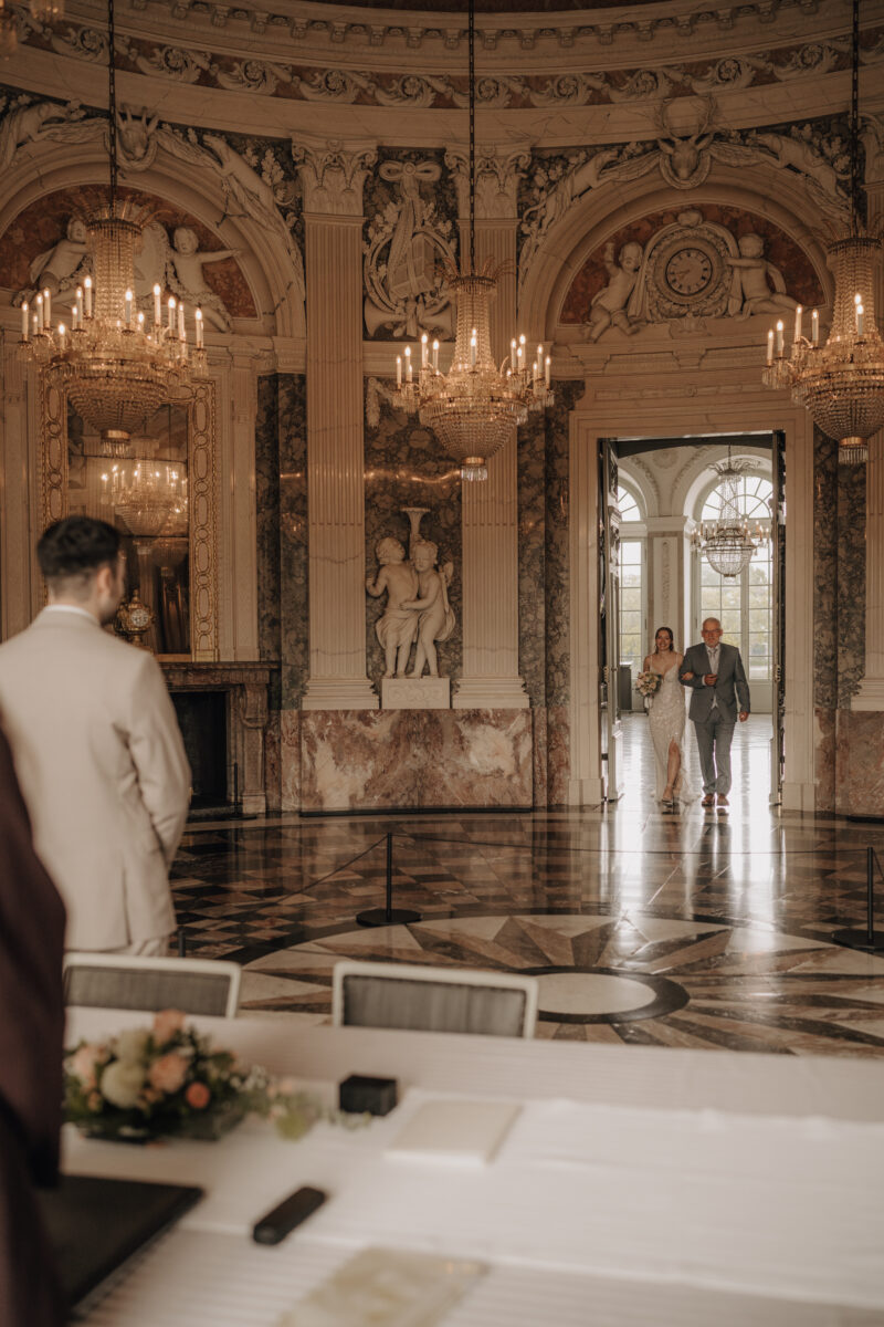 Hochzeitsportfolio, Braut wird vom Brautvater in den Trausaal gebracht, Bräutigam steht am Trautisch