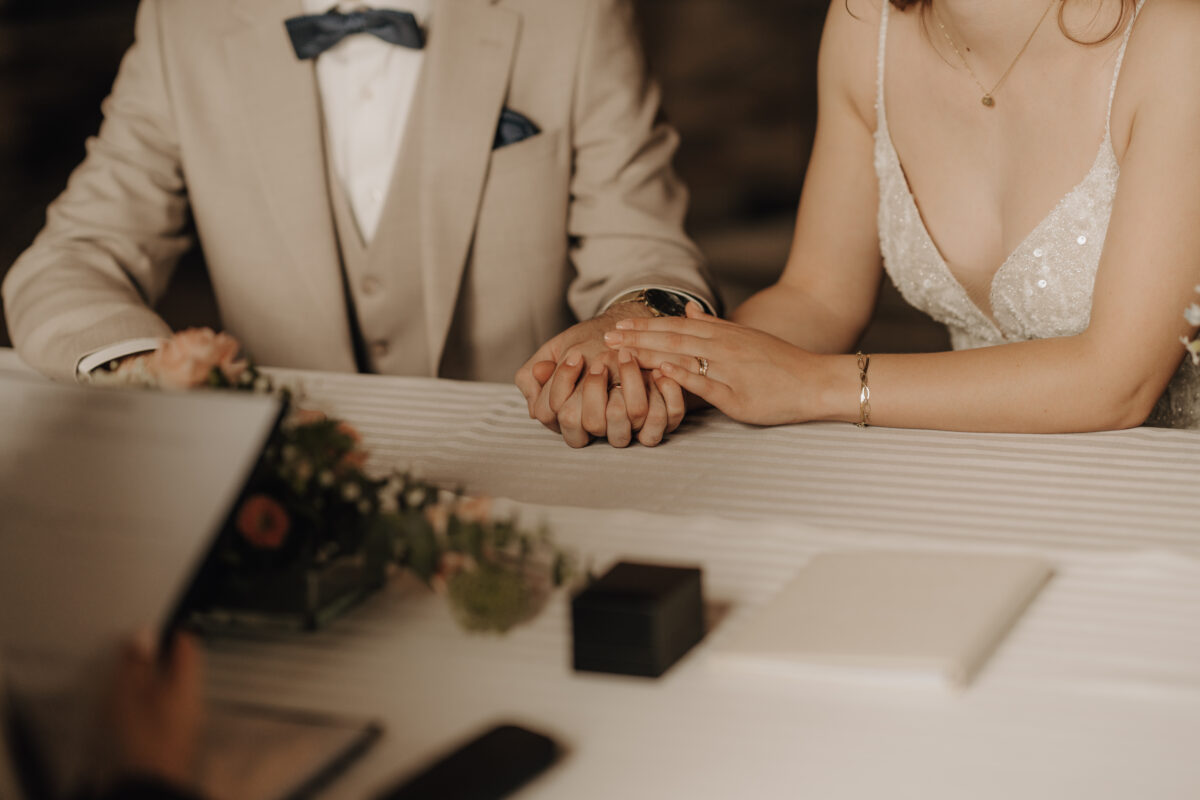 Hochzeitsportfolio, Detailaufnahme bei der standesamtlichen Trauung – Hände des Brautpaares auf dem Trautisch mit Ringen