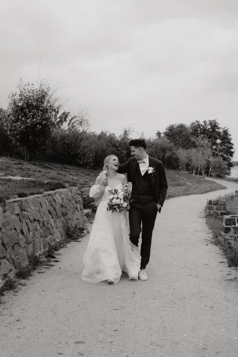 Hochzeitsportfolio, Brautpaar spaziert gemeinsam über einen Weg und lachen sich gegenseitig an | Hochzeitsreportage NRW
