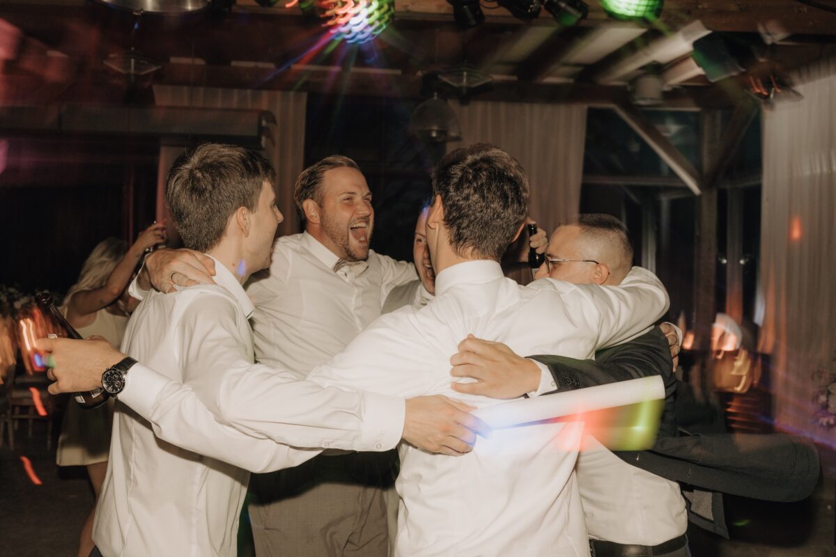 Hochzeitsportfolio, Gäste des Brautpaares am feiern. Alle lachen und halten sich in einem Kreis in den Armen.