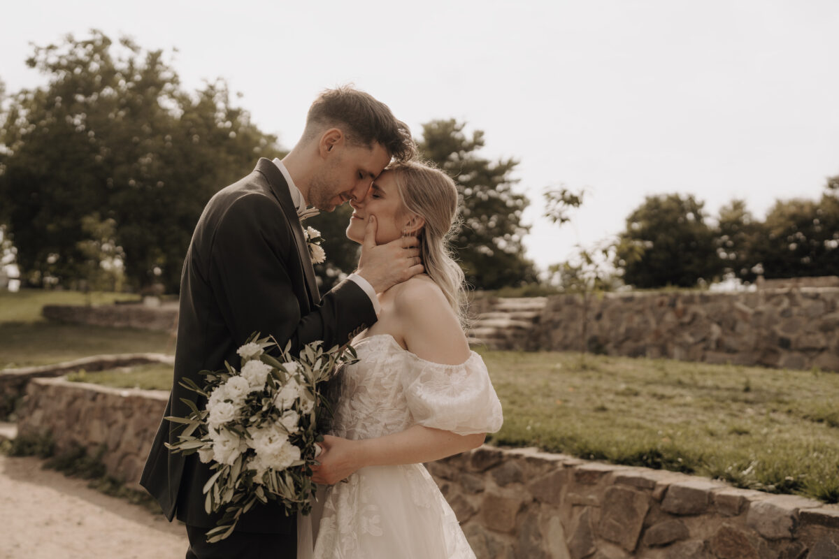 Hochzeitsportfolio, Brautpaar steht gegenüber von einander, Stirn an Stirn, dabei fasst der Bräutigam der Braut in den Nacken und streift mit seinem Daumen über ihre Wange, beide Augen geschlossen