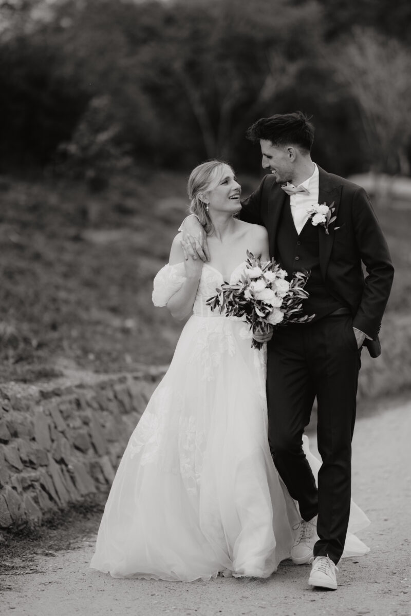 Hochzeitsportfolio, Bräutigam hat einen Arm über die Schulter der Braut geschlungen sie laufen gemeinsam durch die Natur | Hochzeitsfotografin NRW