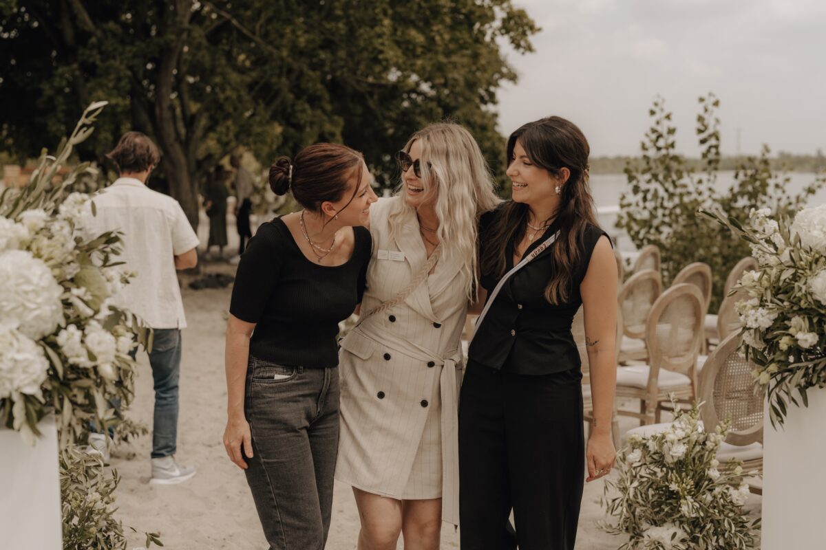 Hochzeitsportfolio, Hochzeitsgäste laufen gemeinsam Arm in Arm auf die Kamera zu und lachen sich gegenseitig an | Hochzeitsfotografie Köln