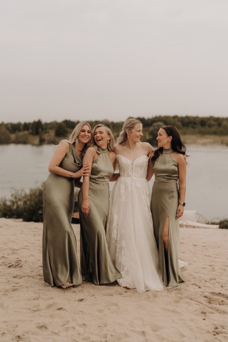 Hochzeitsportfolio, Braut mit ihren Brautjungfern. Die Brautjungfern lachen. Die Braut schaut nach rechts und lächelt ihre Brautjungfer an.