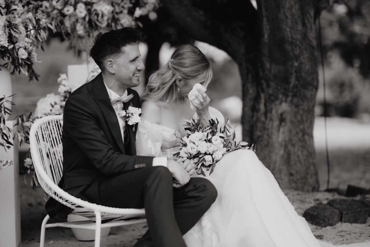 Romantisches Brautpaarporträt unter einem Baum während der Trauung, Braut wischt sich gerde eine Träne weg