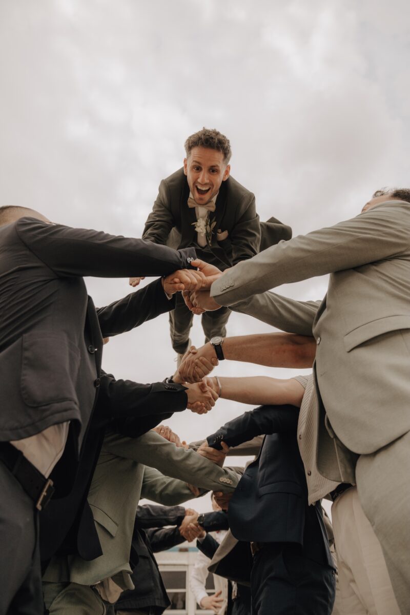 Hochzeitsportfolio, Bräutigam wird von seinen Freundin in die Luft geworfen