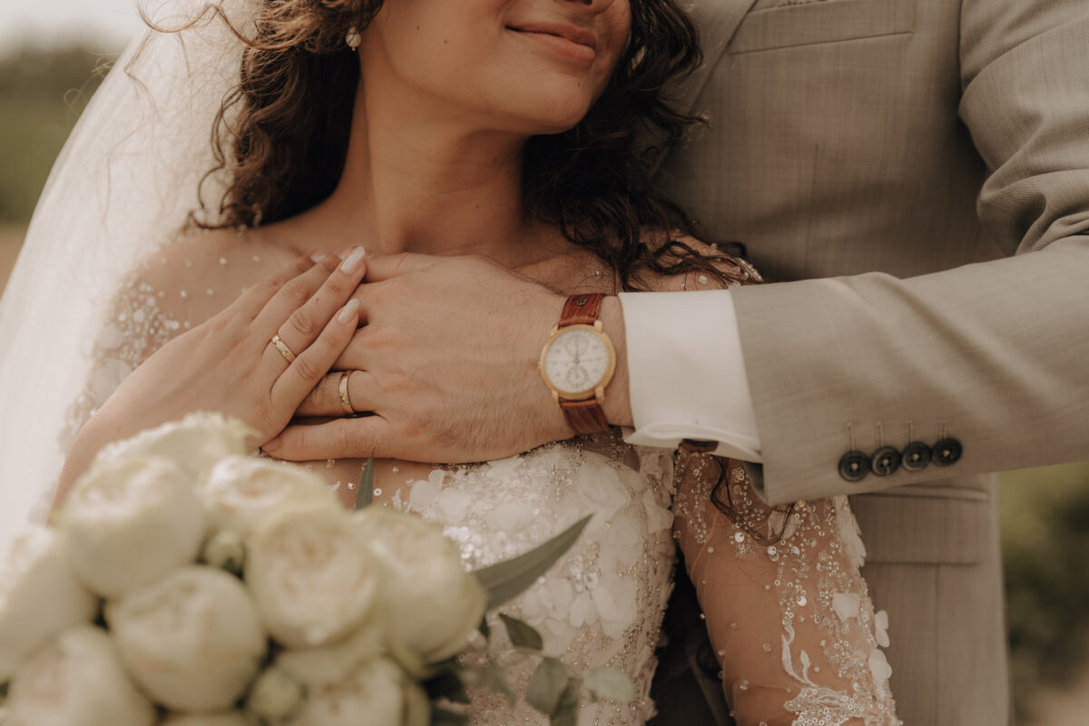 Hochzeitsportfolio, Emotionale Detailaufnahme – Bräutigam umarmt die Braut von hinten, Braut mit Ehering und Uhr des Bräutigams | Hochzeitsreportage NRW