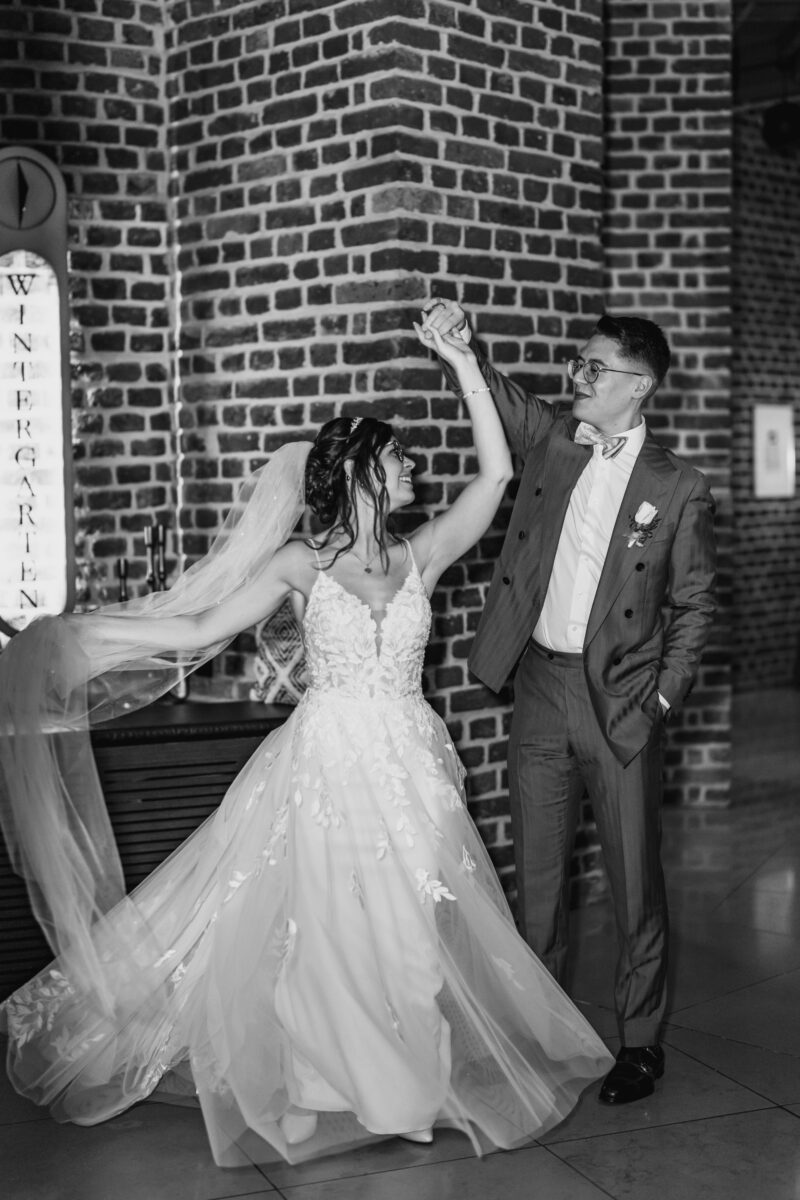 Hochzeitsportfolio, Braut und Bräutigam tanzen zusammen. Er dreht sie in eine Pirouette. Beide lächeln.