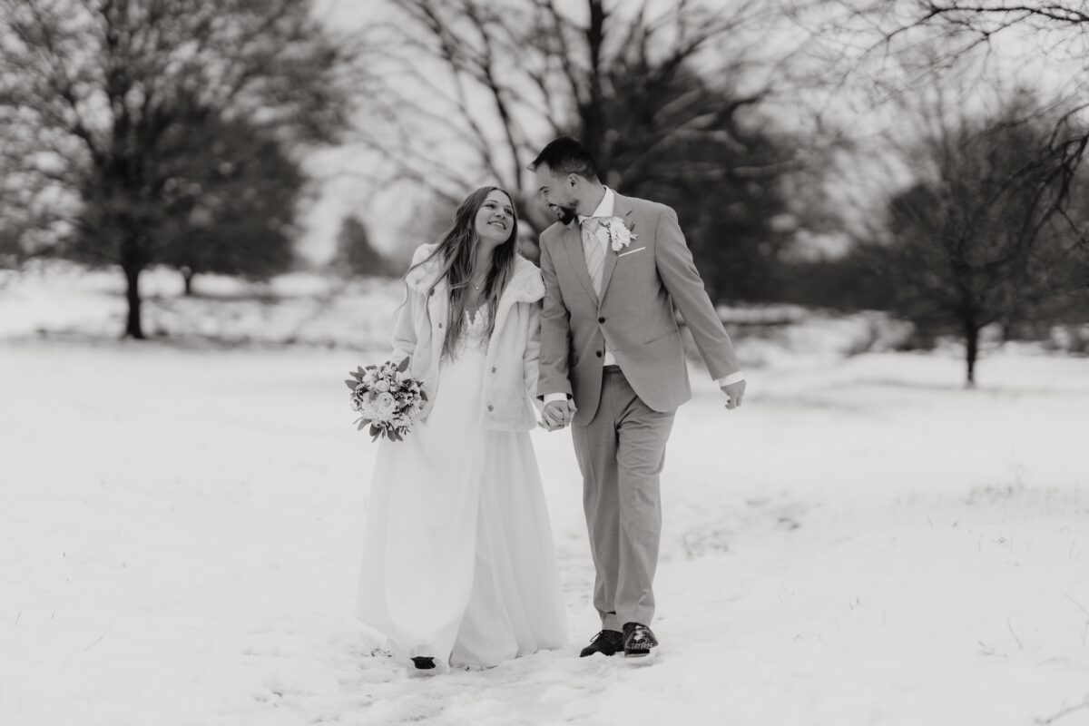 After Wedding Portfolio, Braut und Bräutigam halten sich an der Hand und schauen sich lächelnd an. Sie laufen beide durch den Schnee.