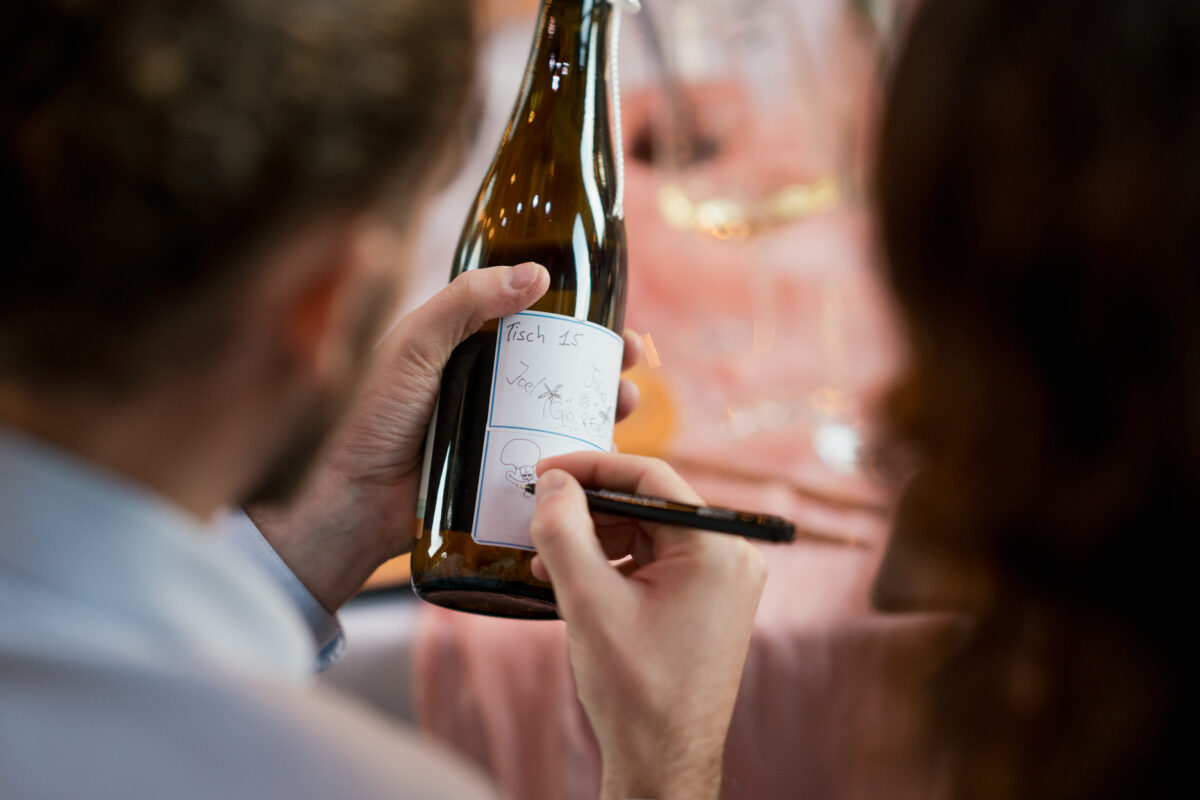 Hochzeitsportfolio, Detailfoto Hochzeitsgast unterschreibt Weinflasche als Erinnerung für das Brautpaar | Hochzeitsreportage NRW