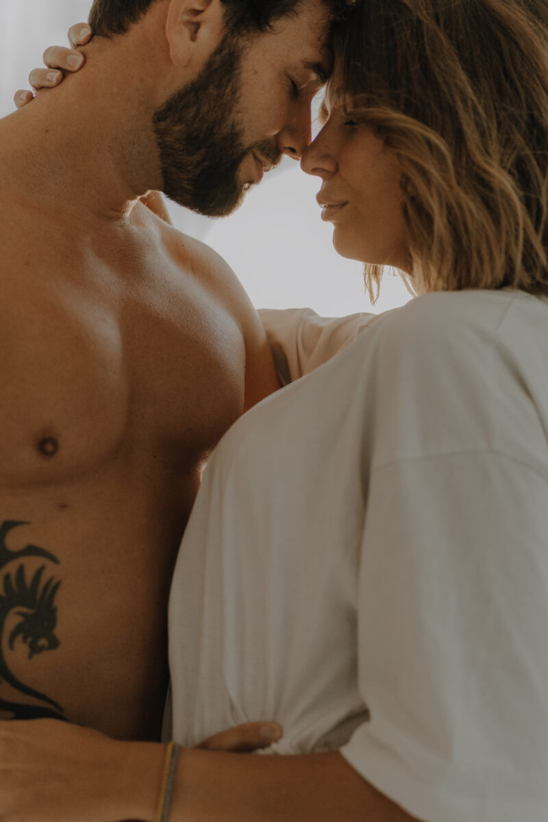 Akt- und Erotikfotografie Portfolio, oberkörperfreier tätowierter Mann und Frau in weißem Hemd halten sich im Arm