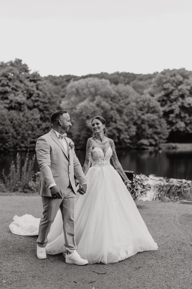 Hochzeitsportfolio, Brautpaar spaziert gemeinsam am See und gucken sich dabei gegenseitig an | Hochzeitsfotografie NRW