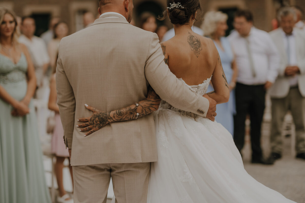 Hochzeitsportfolio, Detailbild vom Brautpaar welches sich seitlich in den Arm nimmt, es wurde von Hinten fotografiert