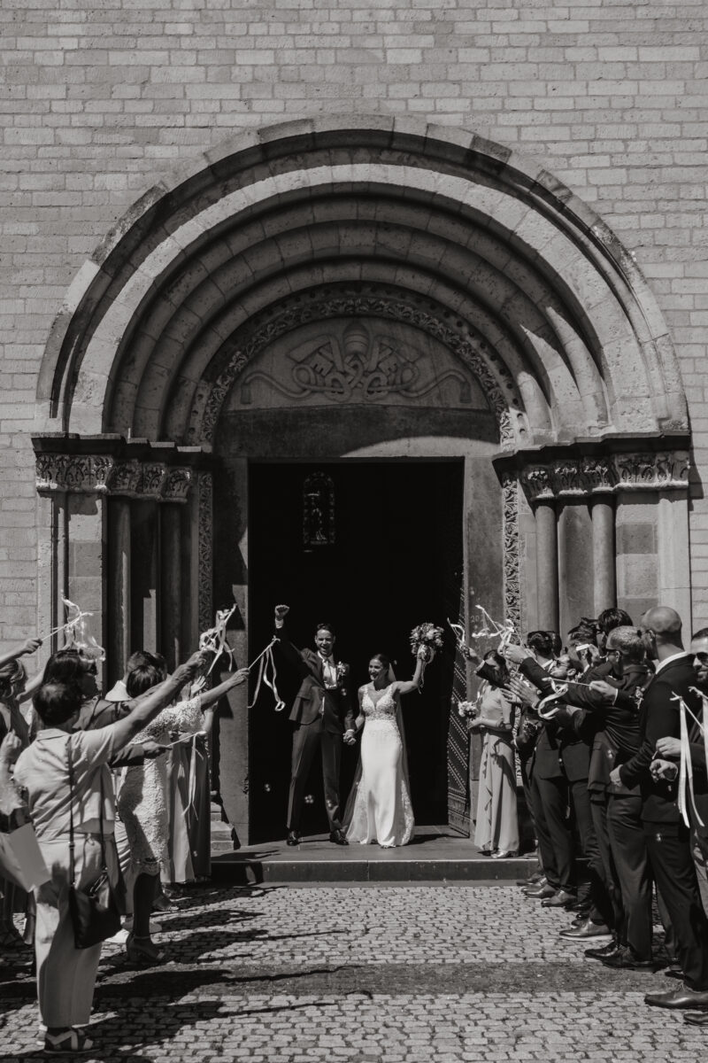 Hochzeitsportfolio, Brautpaar kommen aus der Kirche heraus, Gäste bilden ein Spalier und jubeln mit dem Brautpaar