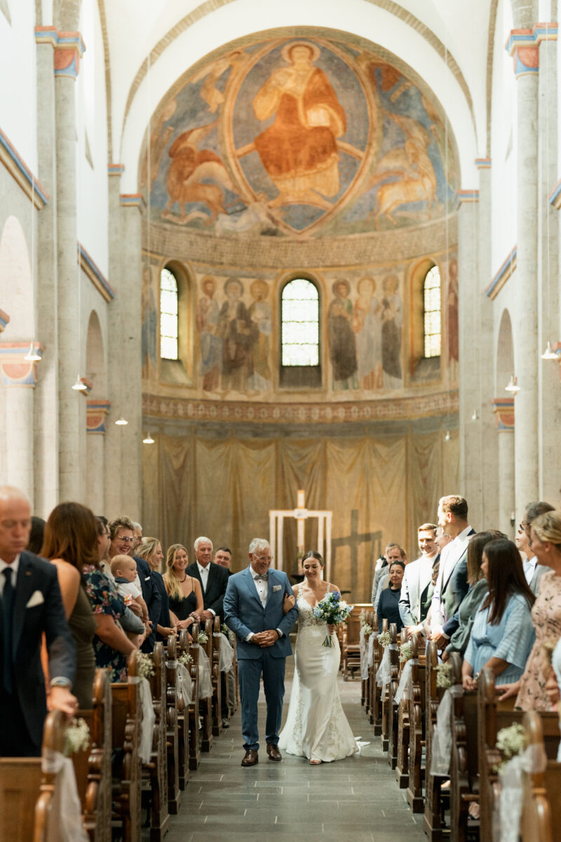 Hochzeitsportfolio, Brautvater führt die Braut durch die Kirche zum Altar durch die Hochzeitsgesellschaft