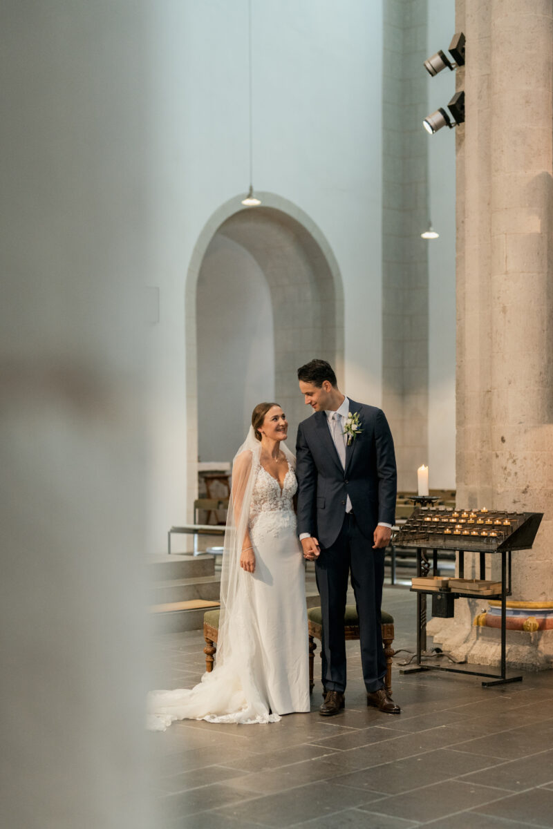 Hochzeitsportfolio, Braut und Bräutigam stehen Hand in Hand am Altar und lächeln sich gegenseitig an