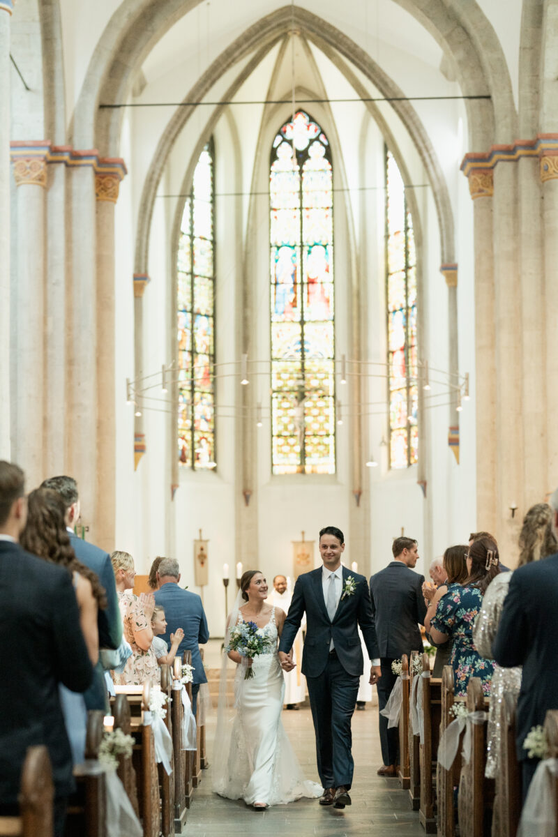 Hochzeitsportfolio, Brautpaar laufen Hand in Hand in der Kirche durch den Gang an ihren Gästen vorbei