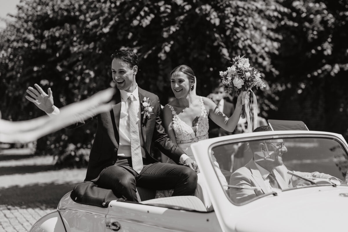 Hochzeitsportfolio, Brautpaar sitzen im Cabrio und jubeln ihren Gästen zu