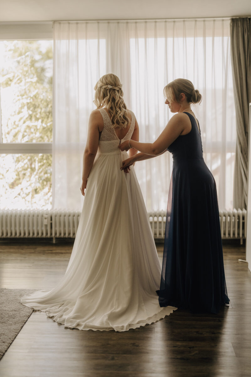 Hochzeitsportfolio, Braut wird beim Getting Ready von einer Freundin beim Ankleiden unterstützt | Hochzeitsreportage NRW