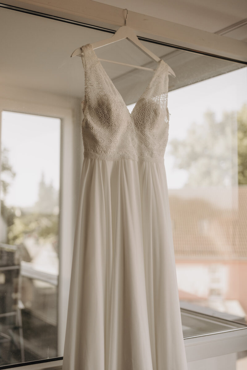 Hochzeitsportfolio, Brautkleid hängt am Fenster im natürlichen Licht beim Getting Ready