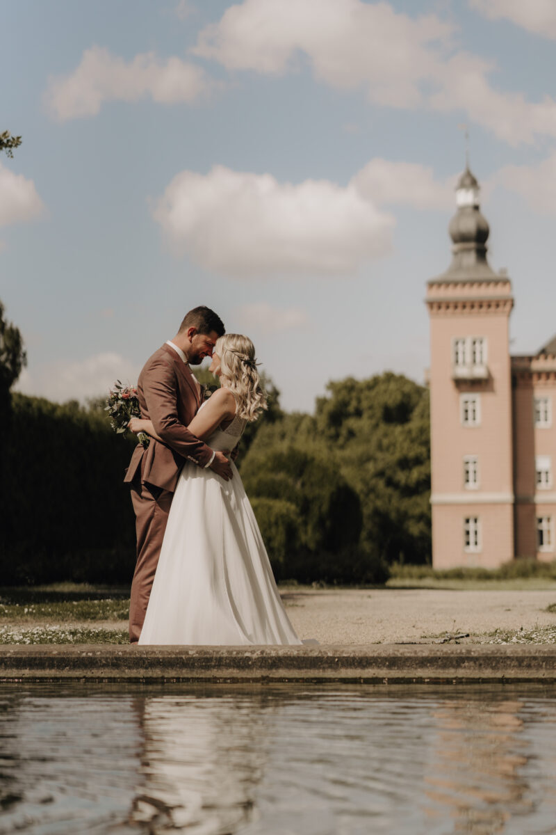 Hochzeitsportfolio, Braut und Bräutigam stehen zusammen. Sie halten sich in den Armen und sind sich ganz nah. Ihre Nasenspitzen berühren sich.