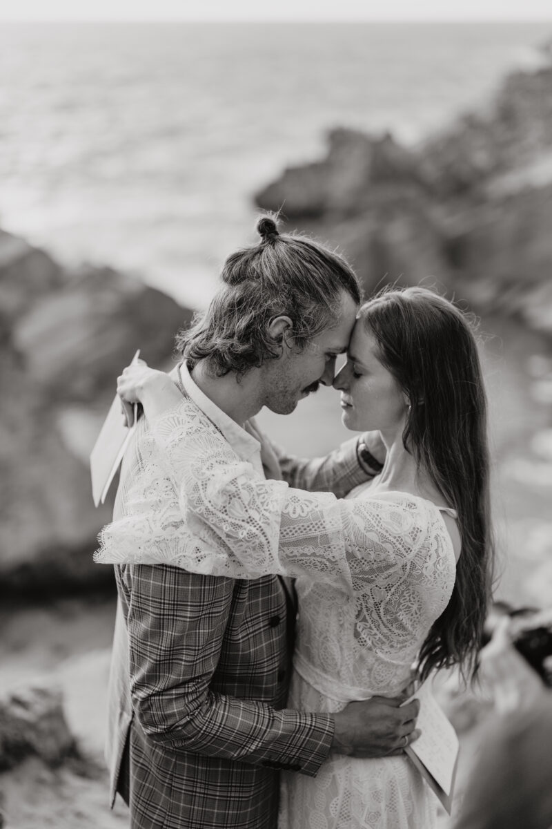 Destination Wedding Portfolio Hochzeitspaar steht sich Stirn an Stirn gegenüber vor Klippen, schwarz-weiß